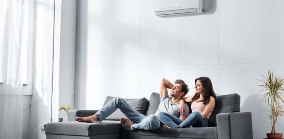 Paar entspannt auf Sofa unter einer Wand-Klimaanlage